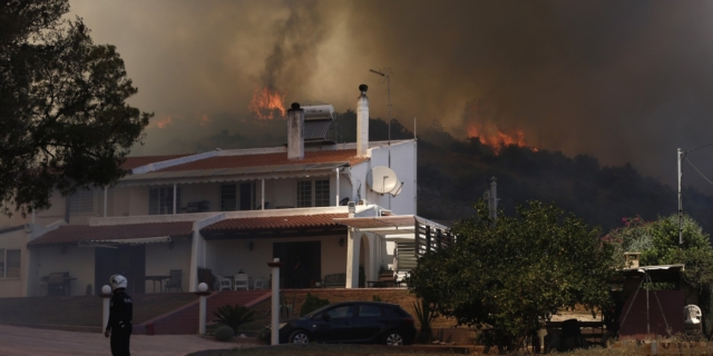 Άνδρας της αστυνομίας στέκεται μπροστά από σπίτι στον οικισμό Κίτσι, κοντά στο σημείο που ξέσπασε πυρκαγιά στην λεωφόρο Βάρης - Κορωπίου