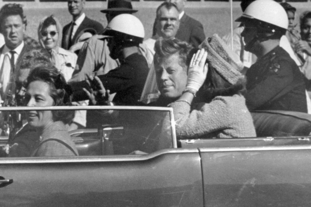 Ο Πρόεδρος Τζον Φ. Κένεντι κουνάει το χέρι από το αυτοκίνητό του σε μια αυτοκινητοπομπή περίπου ένα λεπτό πριν πυροβοληθεί, 22 Νοεμβρίου 1963