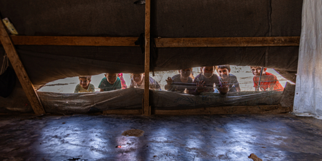 Παιδιά Σύρων προσφύγων ξεπροβάλλουν μέσα από το άνοιγμα εξαερισμού μιας σκηνής.